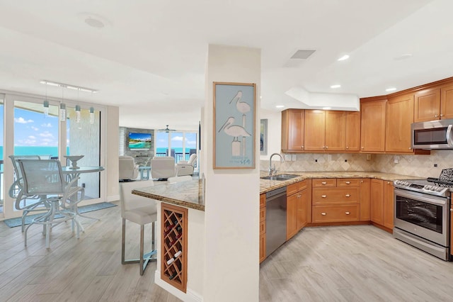 kitchen with appliances with stainless steel finishes, sink, backsplash, light stone counters, and kitchen peninsula