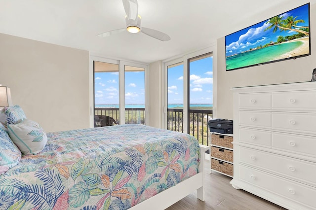 bedroom featuring access to outside, light hardwood / wood-style floors, ceiling fan, and a water view