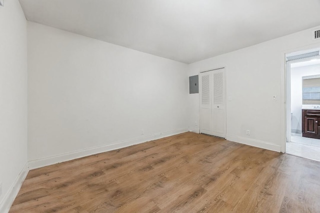 spare room featuring light wood finished floors, visible vents, electric panel, and baseboards