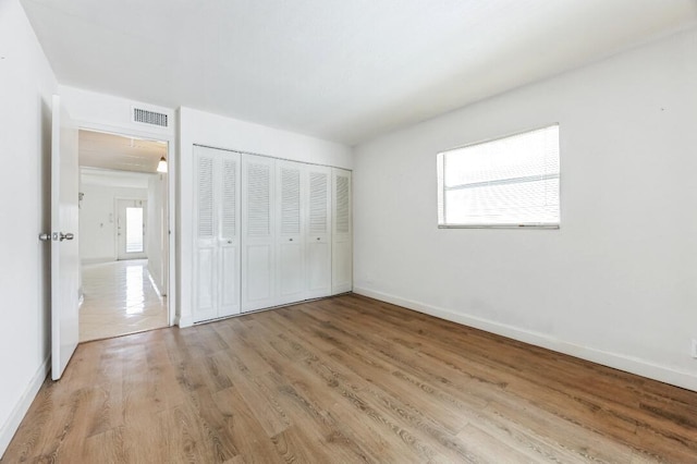 unfurnished bedroom with light wood finished floors, baseboards, visible vents, and a closet