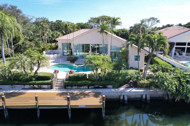 rear view of house with a tiled roof, a patio area, a water view, and an outdoor pool