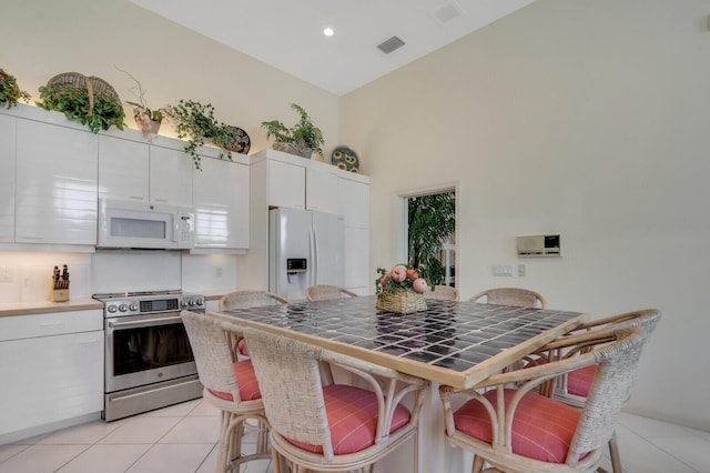 kitchen featuring light countertops, white cabinets, light tile patterned flooring, white appliances, and a kitchen breakfast bar