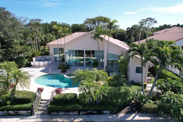 rear view of property with a patio, stucco siding, a tiled roof, and an outdoor pool