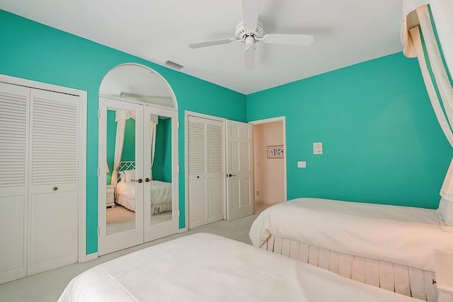 bedroom featuring visible vents, light colored carpet, ceiling fan, french doors, and multiple closets