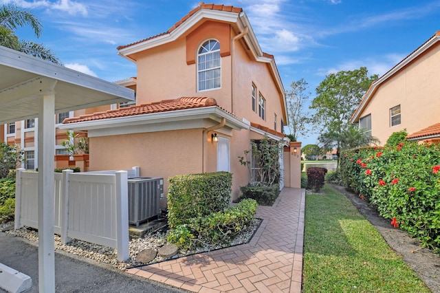 exterior space with central air condition unit, a tiled roof, fence, and stucco siding