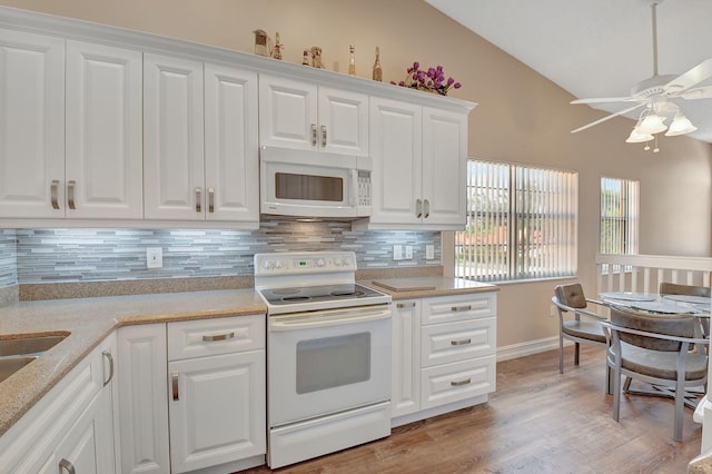 kitchen featuring white appliances, light wood-style flooring, vaulted ceiling, white cabinets, and tasteful backsplash