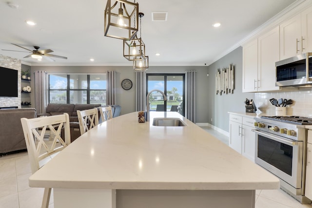 kitchen with a breakfast bar, white cabinets, hanging light fixtures, stainless steel appliances, and a center island with sink