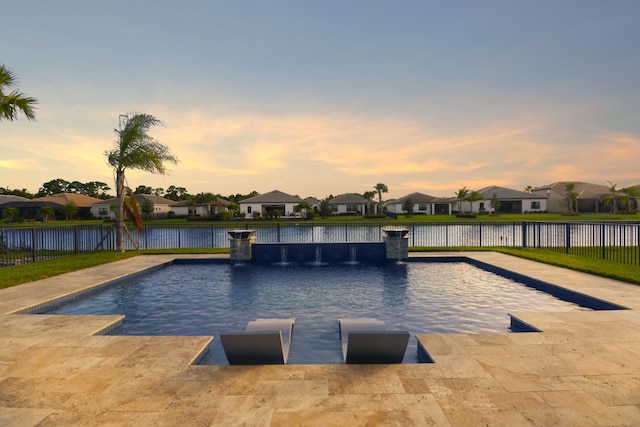 pool at dusk featuring a patio and a water view