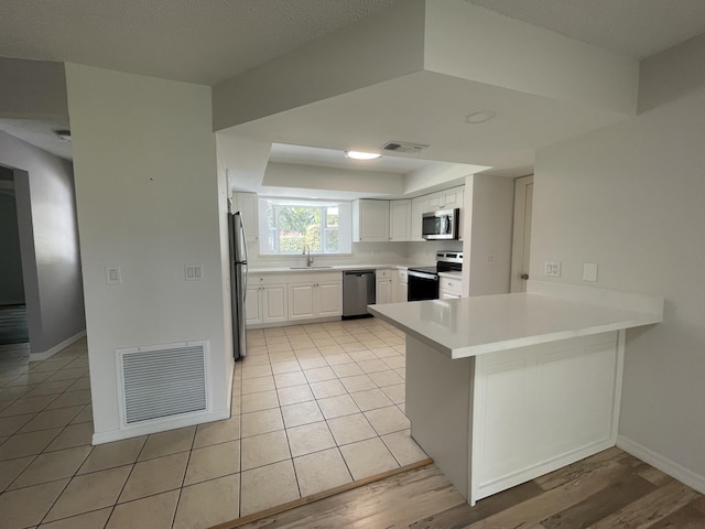 kitchen with sink, light tile patterned floors, appliances with stainless steel finishes, white cabinets, and kitchen peninsula