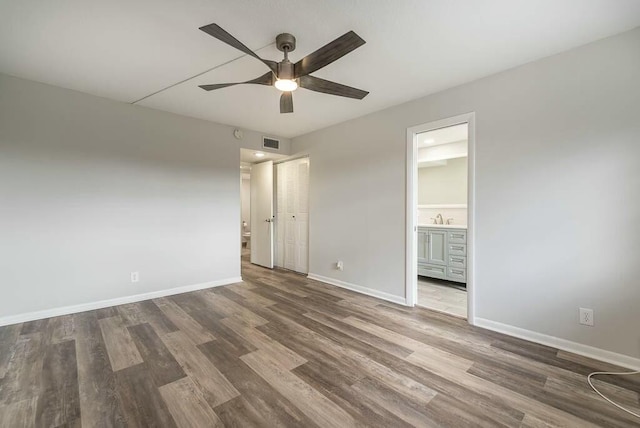 unfurnished bedroom featuring sink, ensuite bath, dark wood-type flooring, ceiling fan, and a closet