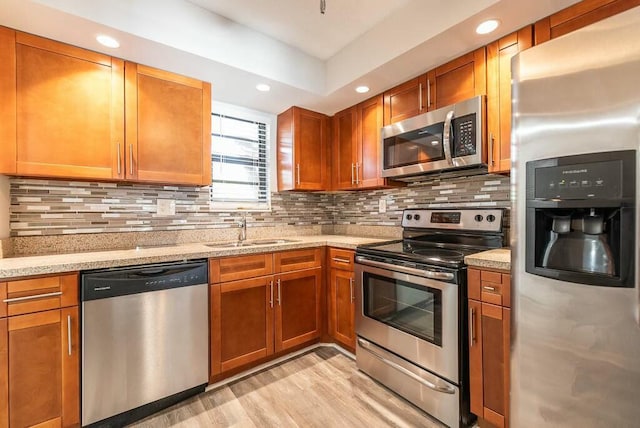 kitchen with appliances with stainless steel finishes, tasteful backsplash, sink, light hardwood / wood-style floors, and light stone countertops