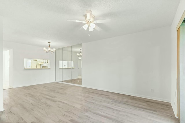 unfurnished living room featuring ceiling fan with notable chandelier, light hardwood / wood-style flooring, and a textured ceiling