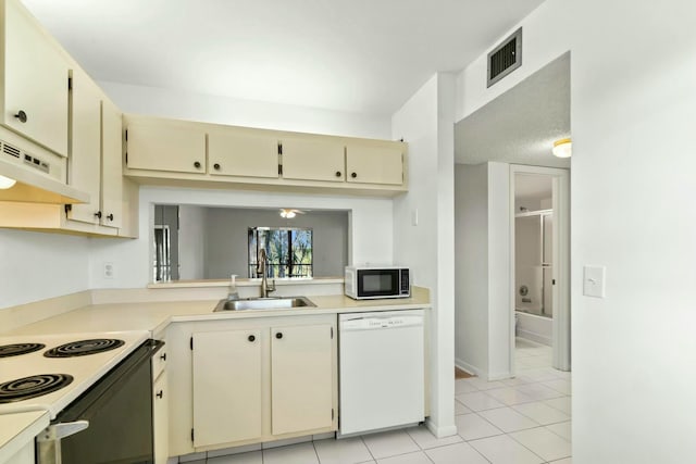 kitchen featuring white dishwasher, sink, light tile patterned floors, and cream cabinetry