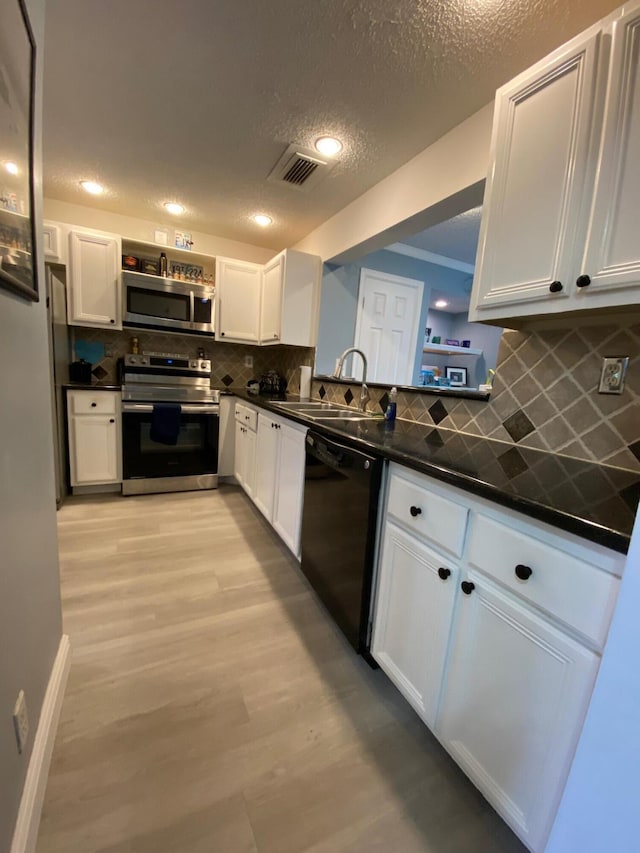 kitchen featuring sink, light wood-type flooring, appliances with stainless steel finishes, white cabinets, and backsplash