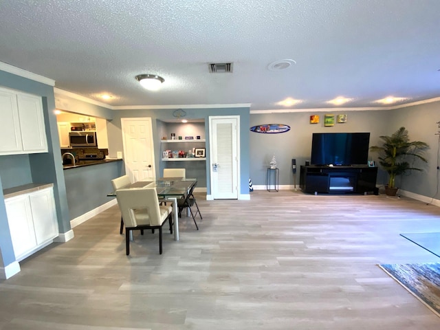 dining room featuring sink, ornamental molding, light hardwood / wood-style floors, and a textured ceiling