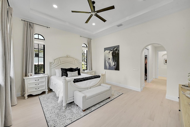 bedroom with a raised ceiling, light hardwood / wood-style floors, and multiple windows