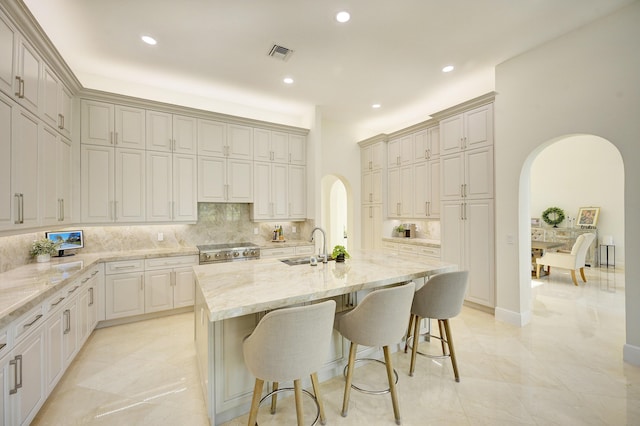 kitchen featuring sink, a breakfast bar area, a kitchen island with sink, light stone counters, and stainless steel range oven