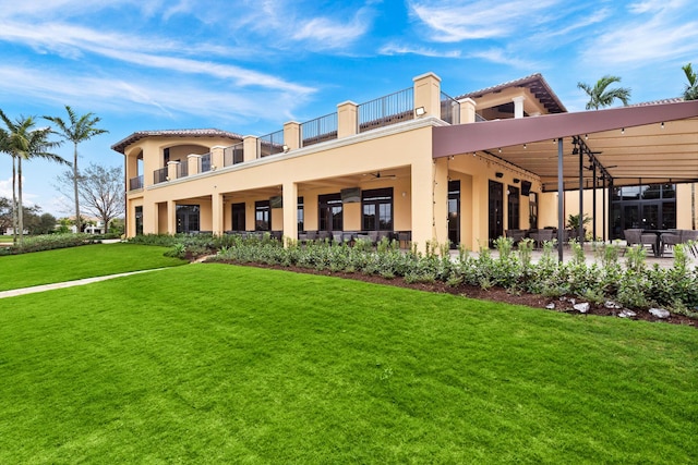 back of property with ceiling fan, a balcony, a patio, and a lawn