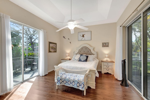 bedroom featuring a tray ceiling, access to outside, dark hardwood / wood-style floors, and ceiling fan