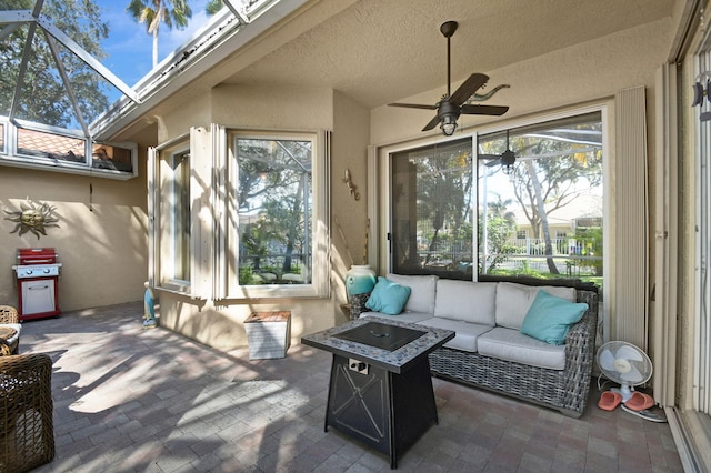 view of patio with ceiling fan, an outdoor living space with a fire pit, and glass enclosure