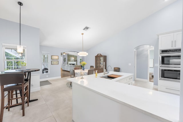 kitchen featuring stainless steel double oven, arched walkways, a sink, light countertops, and white cabinets