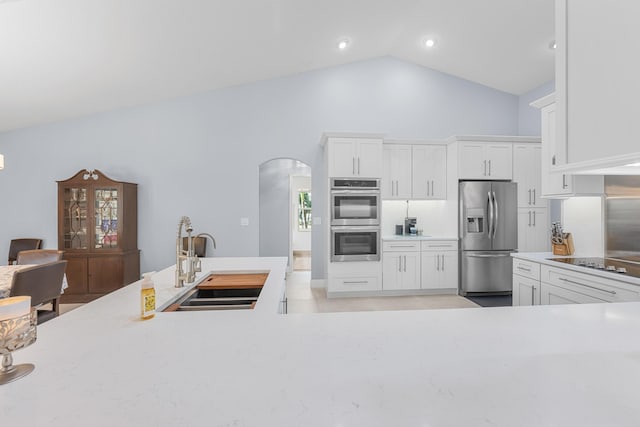 kitchen with high vaulted ceiling, a sink, stainless steel appliances, arched walkways, and white cabinets