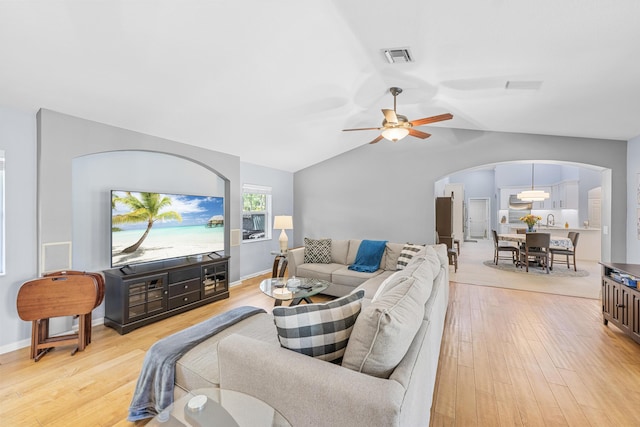 living room featuring visible vents, light wood-style flooring, a ceiling fan, arched walkways, and vaulted ceiling