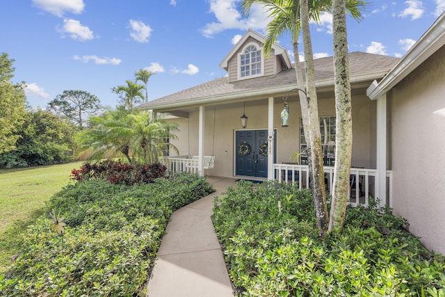 doorway to property featuring covered porch and a lawn