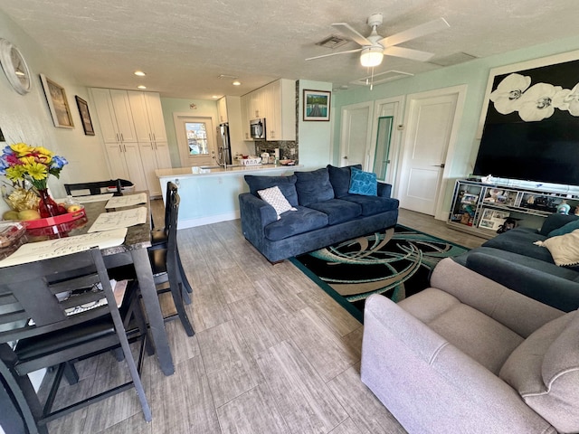 living room featuring ceiling fan, light wood-type flooring, and a textured ceiling