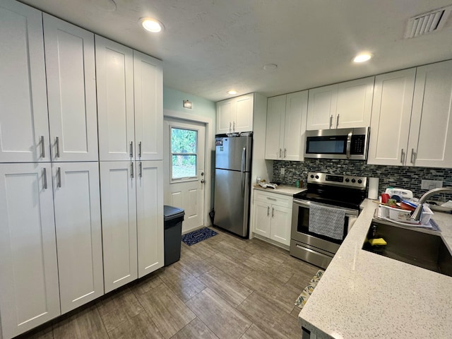 kitchen featuring tasteful backsplash, stainless steel appliances, light stone countertops, and white cabinets