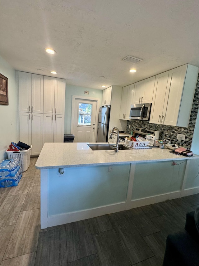 kitchen with white cabinetry, appliances with stainless steel finishes, dark hardwood / wood-style floors, and kitchen peninsula