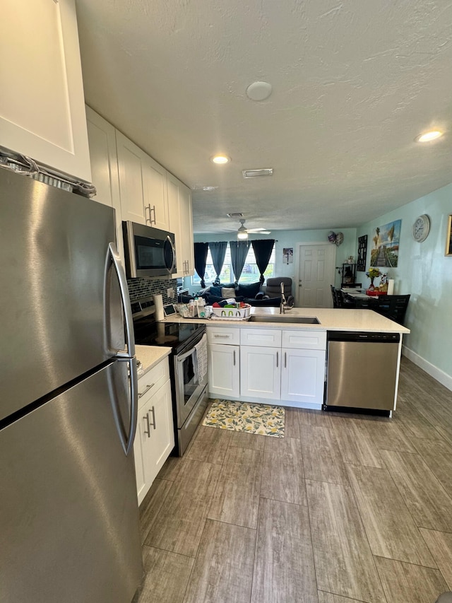 kitchen featuring sink, kitchen peninsula, stainless steel appliances, decorative backsplash, and white cabinets