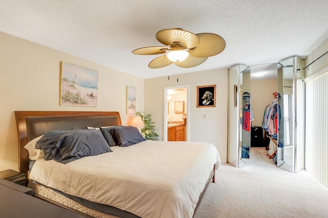 bedroom with ensuite bathroom, a spacious closet, light carpet, a textured ceiling, and a closet