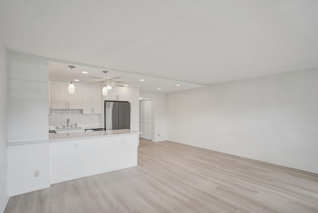 kitchen featuring white cabinetry, decorative light fixtures, stainless steel fridge, kitchen peninsula, and light hardwood / wood-style floors