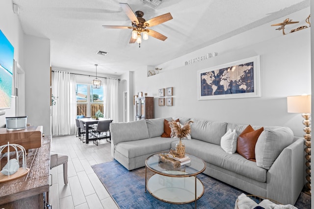 living room with ceiling fan, a textured ceiling, and light wood-type flooring