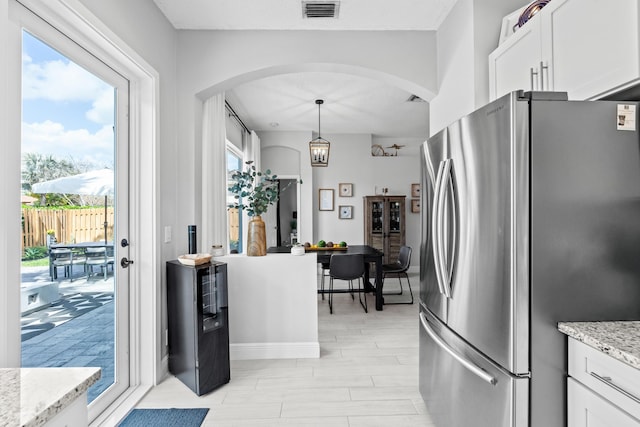 kitchen with white cabinets, light stone countertops, pendant lighting, and stainless steel fridge