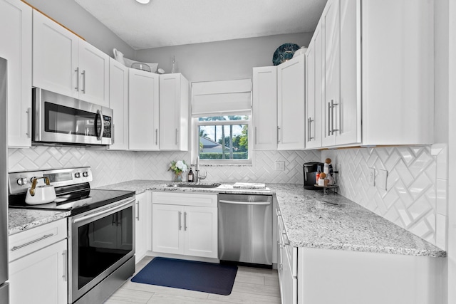 kitchen featuring sink, backsplash, white cabinets, light stone counters, and stainless steel appliances