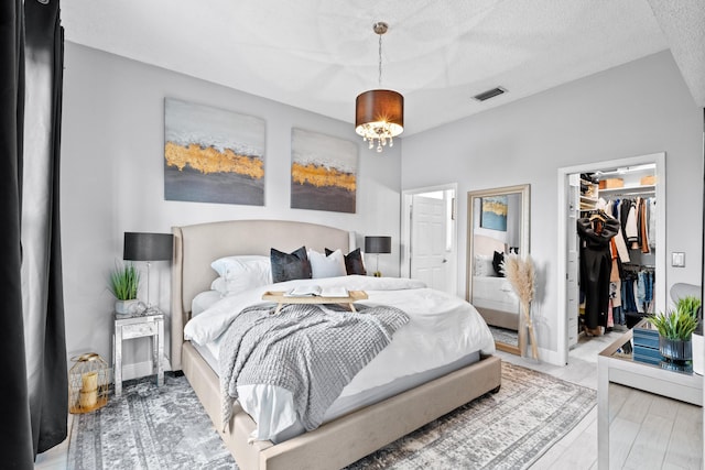 bedroom with hardwood / wood-style flooring, an inviting chandelier, a textured ceiling, a walk in closet, and a closet