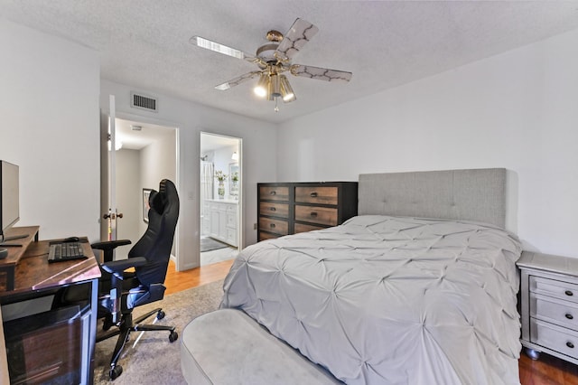 bedroom featuring ceiling fan, ensuite bath, light hardwood / wood-style floors, and a textured ceiling