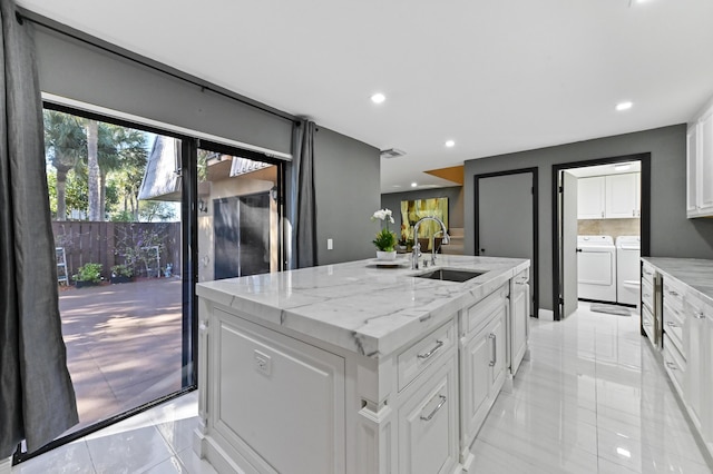 kitchen with separate washer and dryer, sink, white cabinets, light stone counters, and a center island with sink