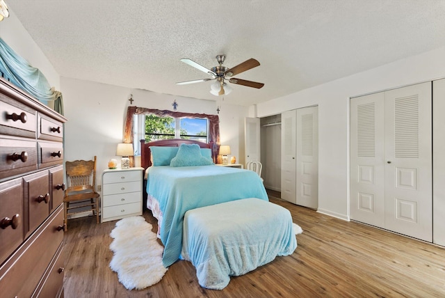 bedroom featuring hardwood / wood-style floors, two closets, a textured ceiling, and ceiling fan