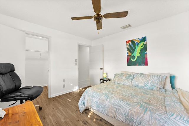 bedroom with wood-type flooring, a walk in closet, ceiling fan, and a closet