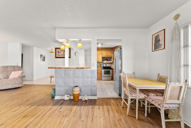 kitchen with appliances with stainless steel finishes, a textured ceiling, light hardwood / wood-style flooring, and backsplash