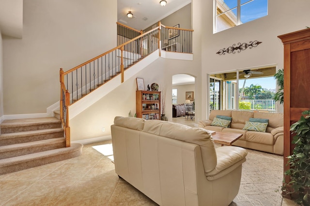 living area with arched walkways, light tile patterned floors, a towering ceiling, baseboards, and stairway