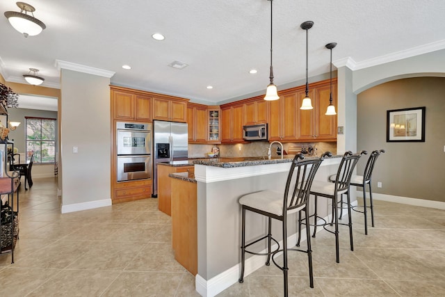 kitchen with appliances with stainless steel finishes, pendant lighting, dark stone countertops, backsplash, and light tile patterned floors