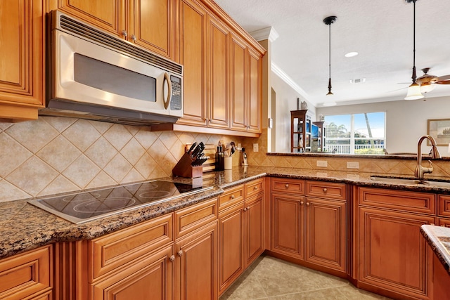 kitchen featuring sink, black electric stovetop, dark stone counters, and decorative light fixtures