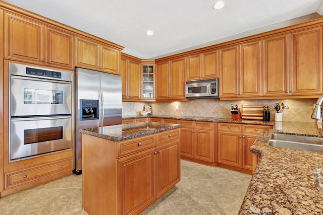 kitchen with stainless steel appliances, a sink, brown cabinets, dark stone counters, and tasteful backsplash