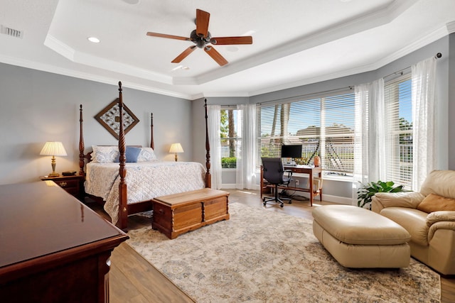 bedroom with crown molding, light hardwood / wood-style flooring, ceiling fan, and a tray ceiling