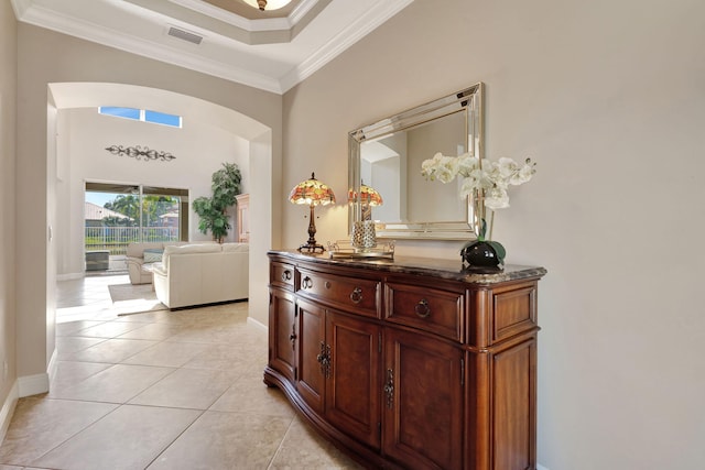 hallway with crown molding, a towering ceiling, a tray ceiling, and light tile patterned floors