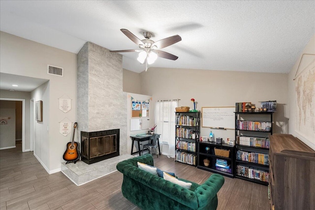 living area with lofted ceiling, ceiling fan, a tile fireplace, and a textured ceiling